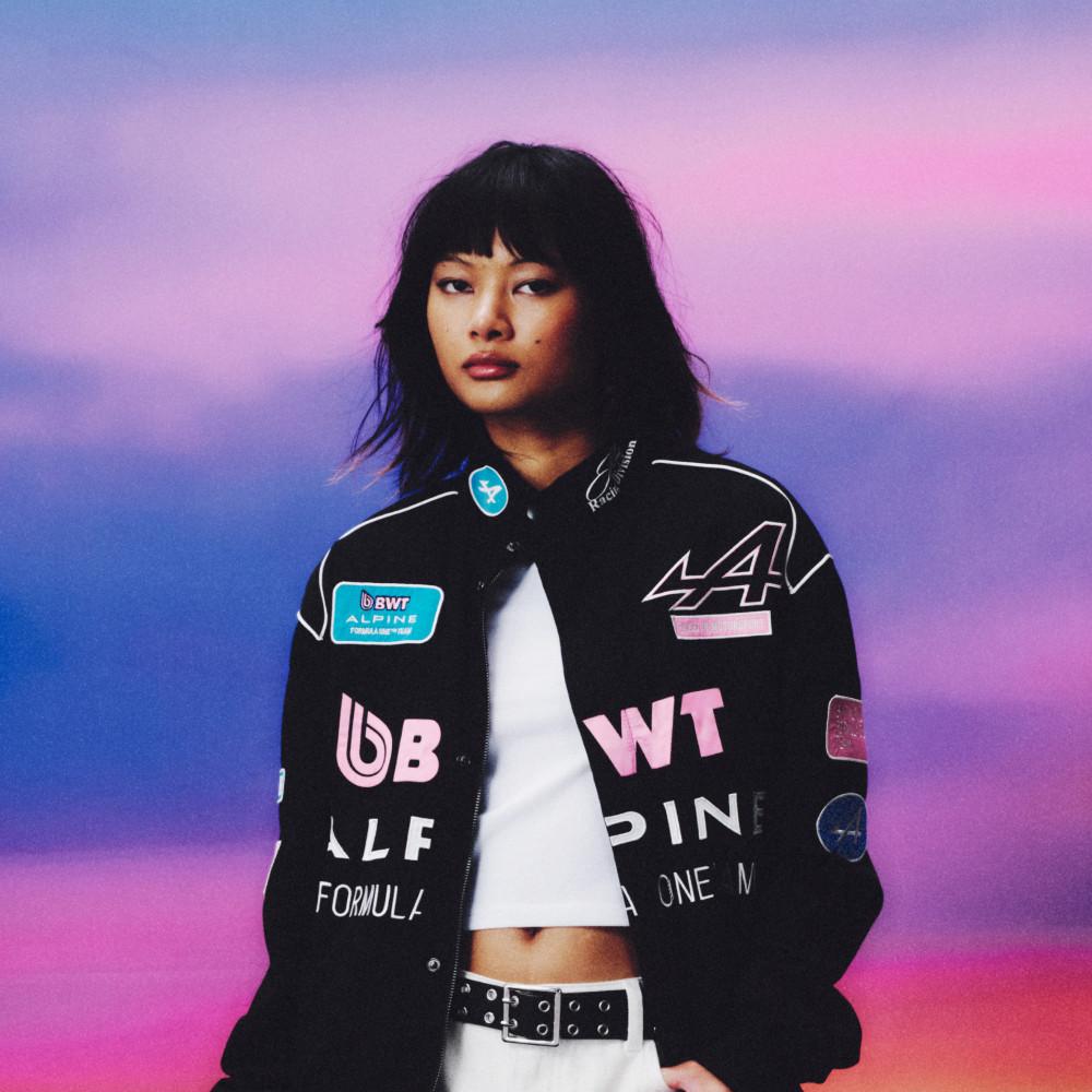 Mannequin portant une veste de course noire BWT Alpine Formula One Team avec logo, détails et écussons roses.