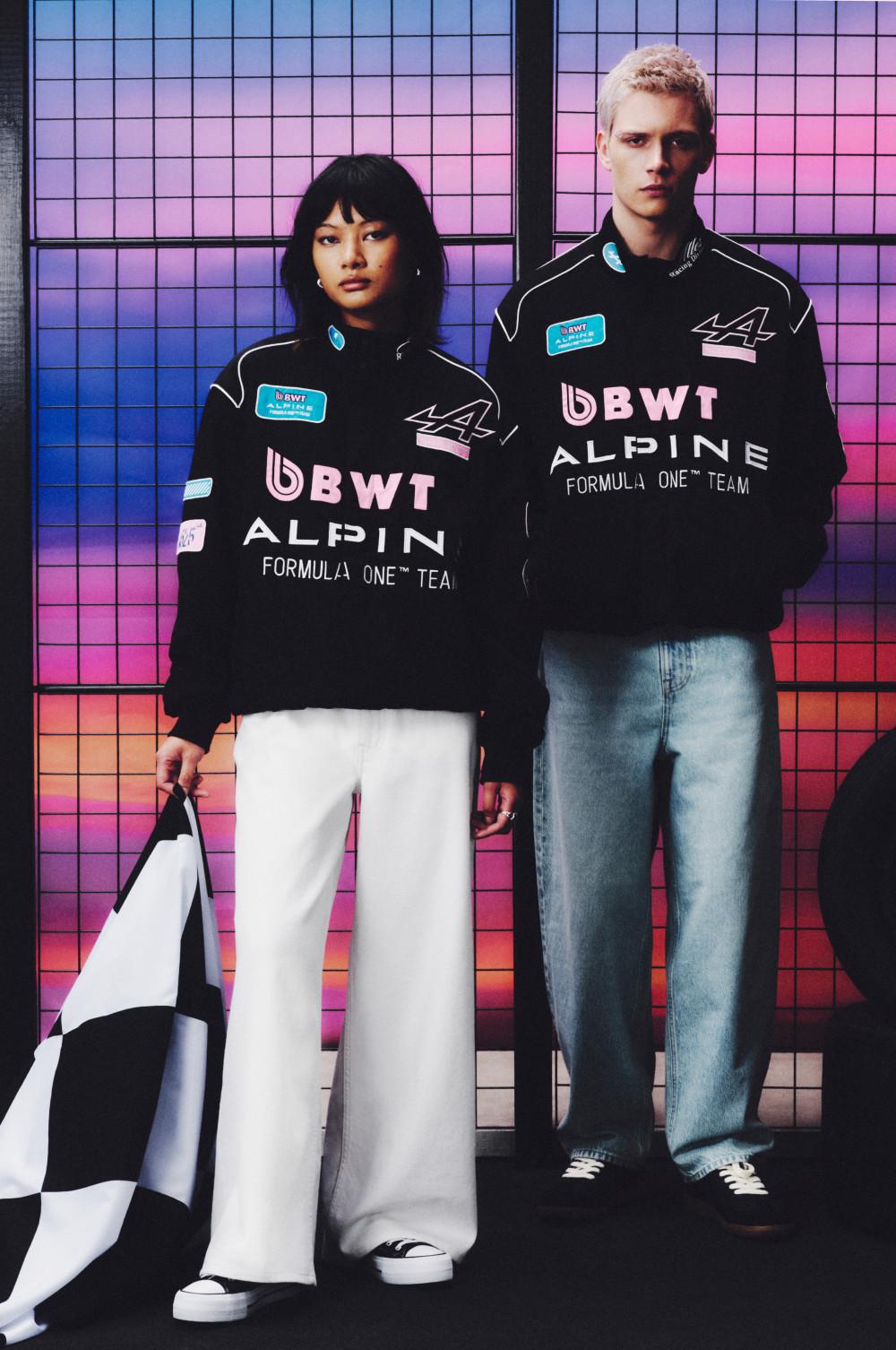 Deux mannequins portant des sweat-shirts noirs BWT Alpine Formula One Team devant un fond à carreaux coloré.