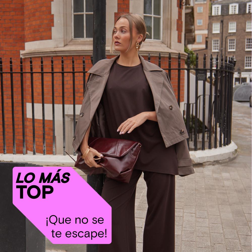 Persona con un conjunto marrón, una gabardina beis y un bolso de mano de piel color burdeos en la calle de una ciudad. Etiqueta rosa «MAJOR FIND» visible en la foto.