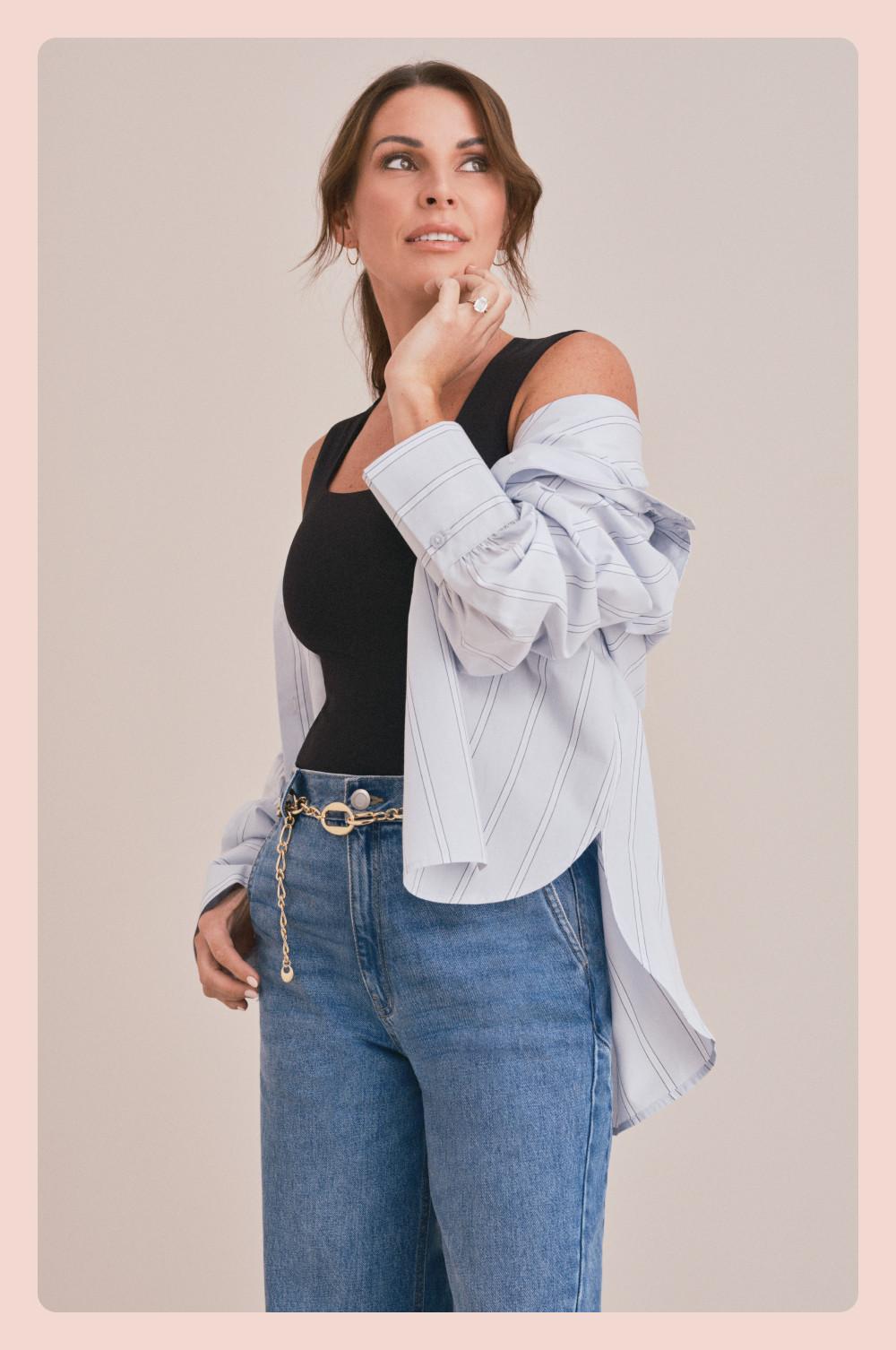 Coleen Rooney wearing black sleeveless top, light blue shirt draped over shoulders, and blue jeans with chain belt.