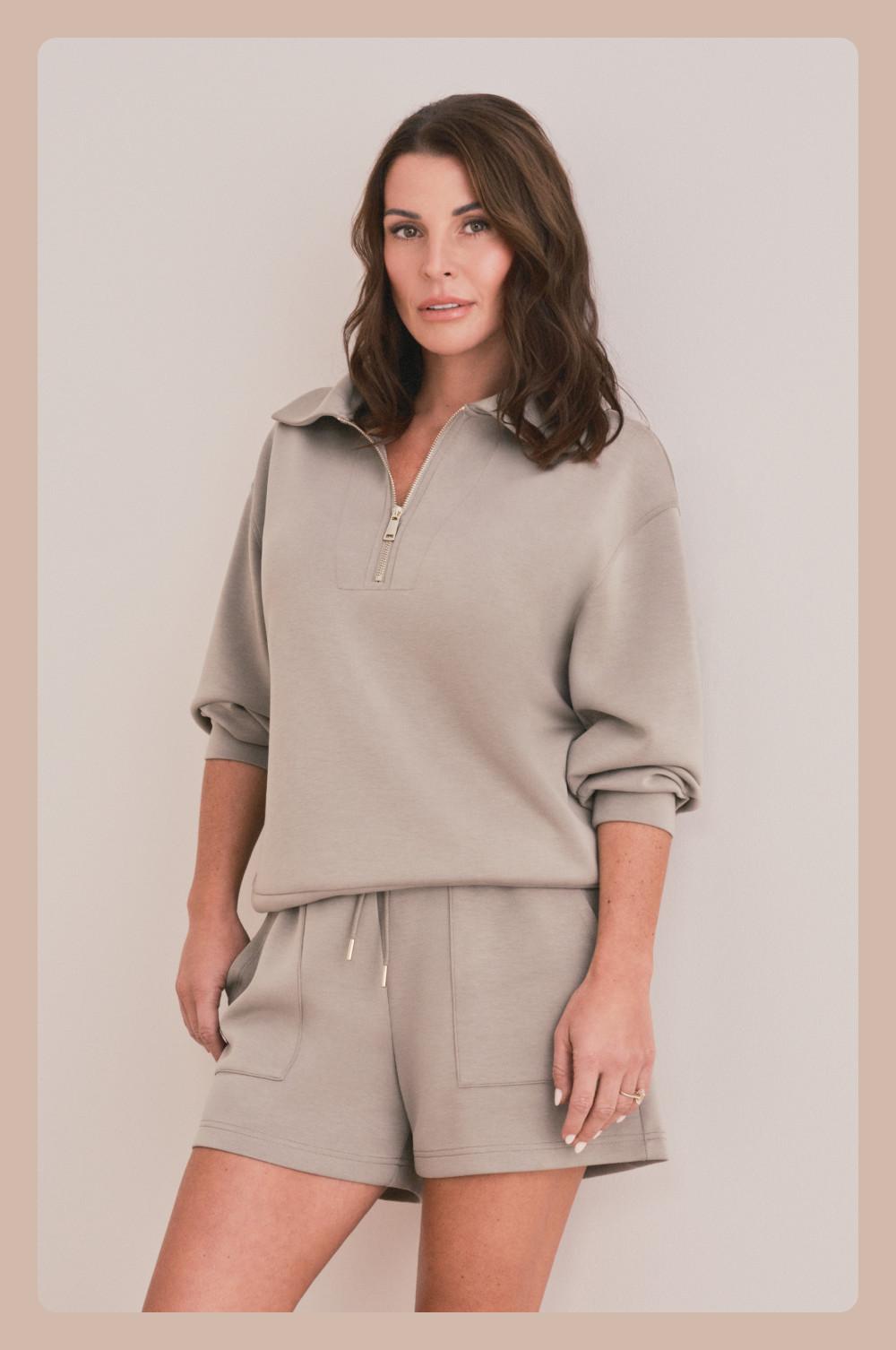 Coleen Rooney wearing a beige half-zip sweatshirt and matching drawstring shorts in a coordinating loungewear set.