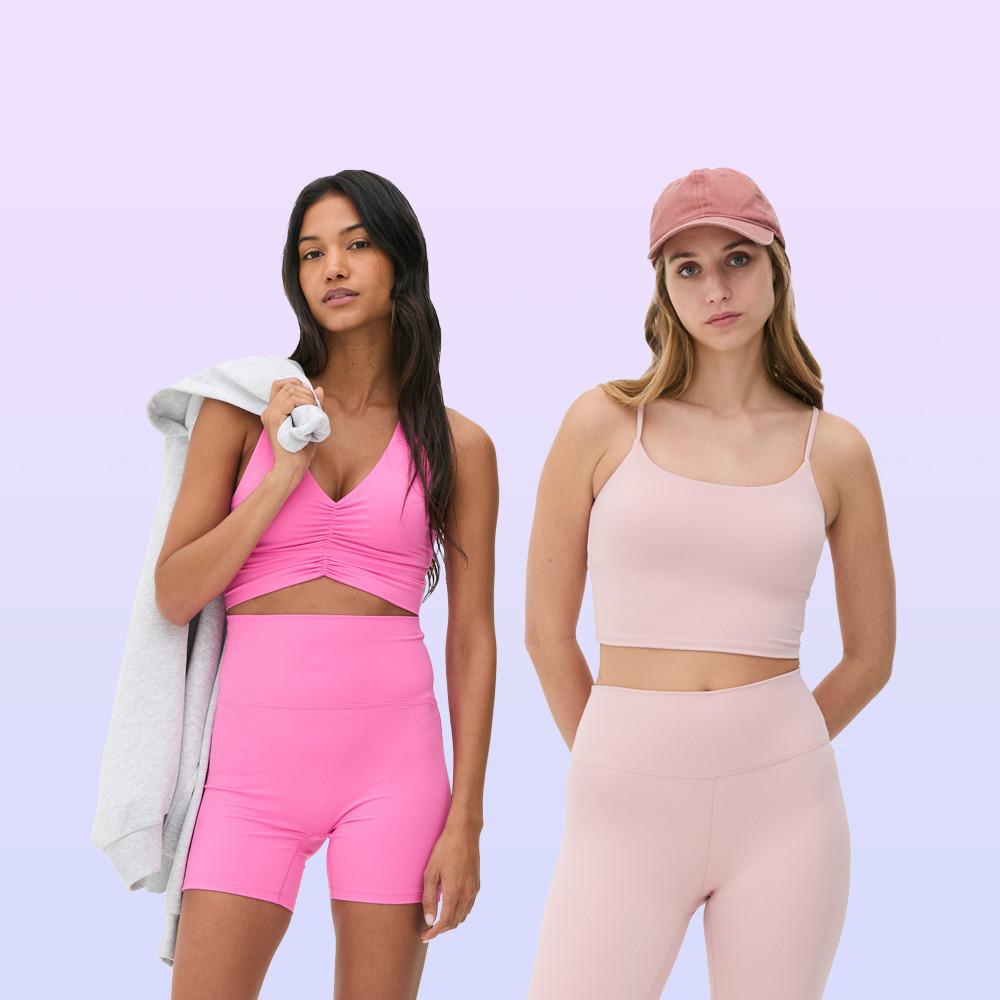Two models wearing athletic apparel: bright pink crop top and shorts with grey sweatshirt, and blush pink crop top and leggings with matching cap.