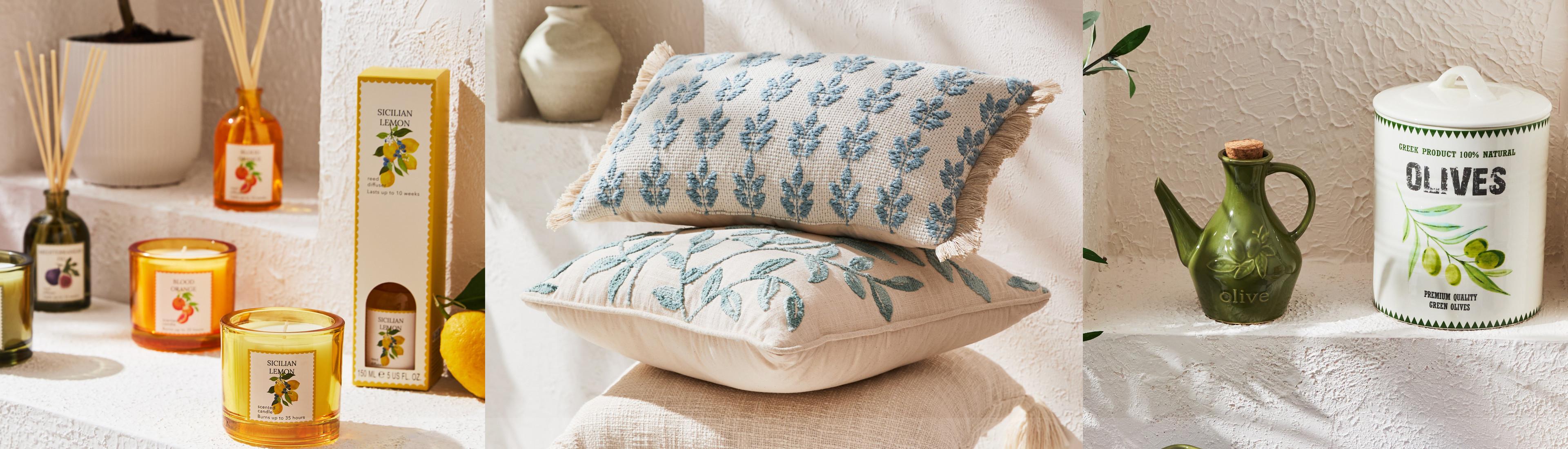 Arredi per la casa ispirati a uno stile mediterraneo, tra cui cuscini ricamati sovrapposti, candele ai limoni siciliani e ceramiche a tema olive.