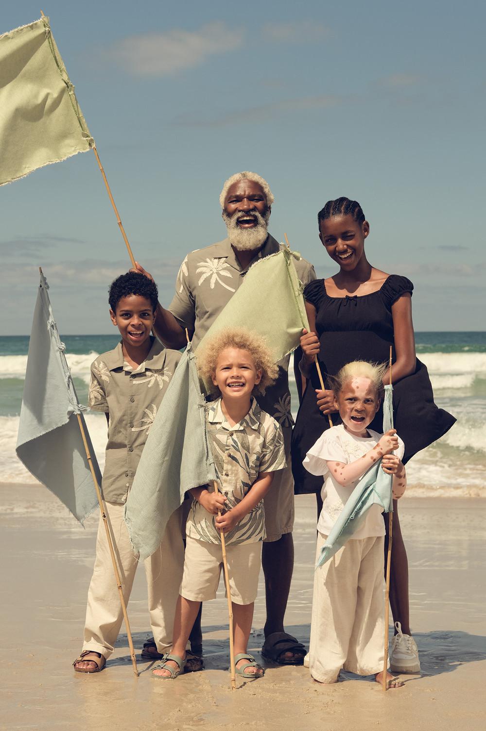 Familie, die gemeinsam an einem sonnigen Strand mit Meereswellen im Hintergrund steht und Stofffahnen hält.