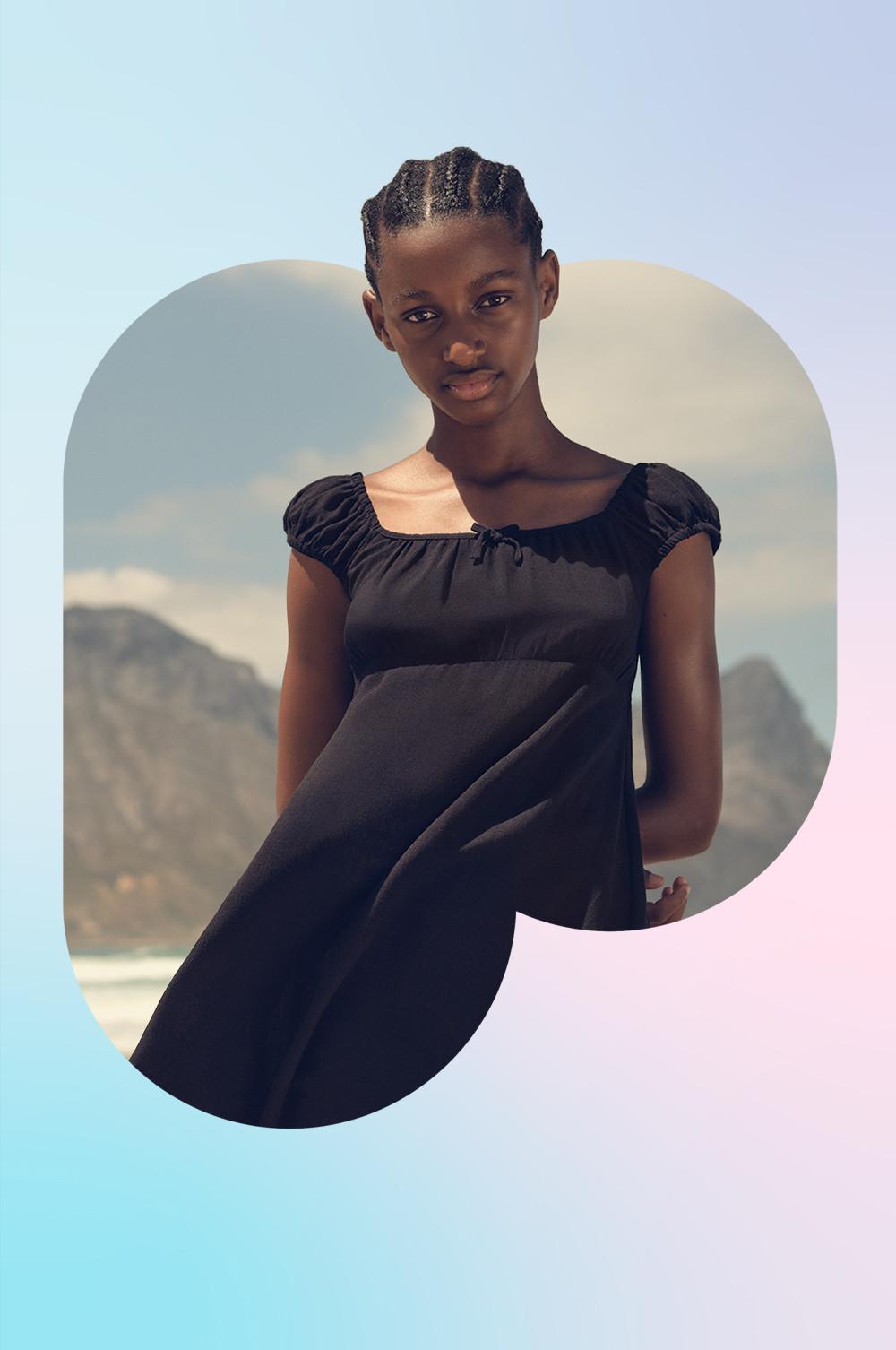 Schwarzes Baumwollkleid mit gerafftem Ausschnitt und Flügelärmeln, fotografiert am Strand mit Meereswellen im Hintergrund.