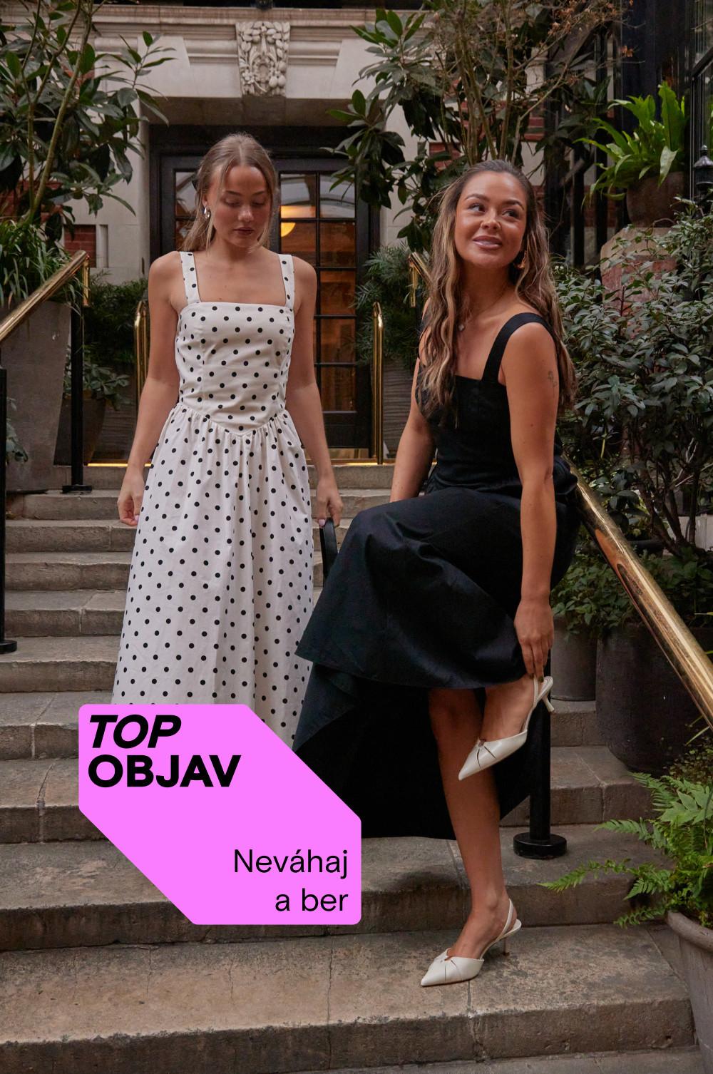 Dve modelky stoja na schodoch. Jedna má oblečené biele bodkované šaty a druhá čierne v kombinácii s bielymi topánkami.