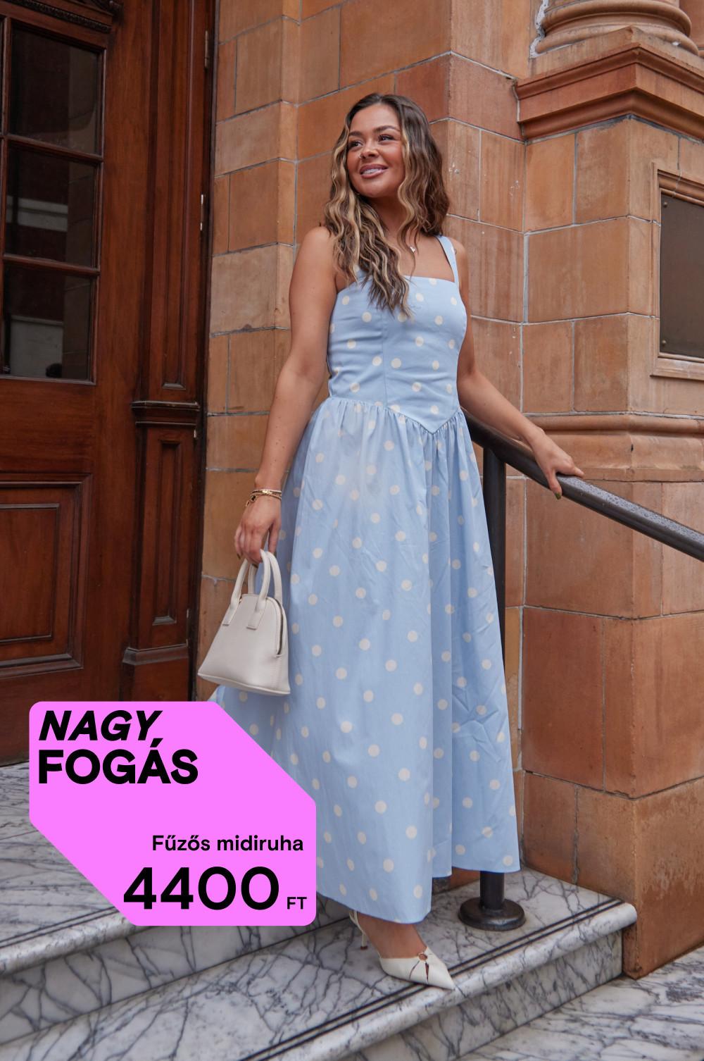 A kőlépcsőn álló modell világoskék pöttyös, fűzős midiruhát visel krémszínű kézitáskával.