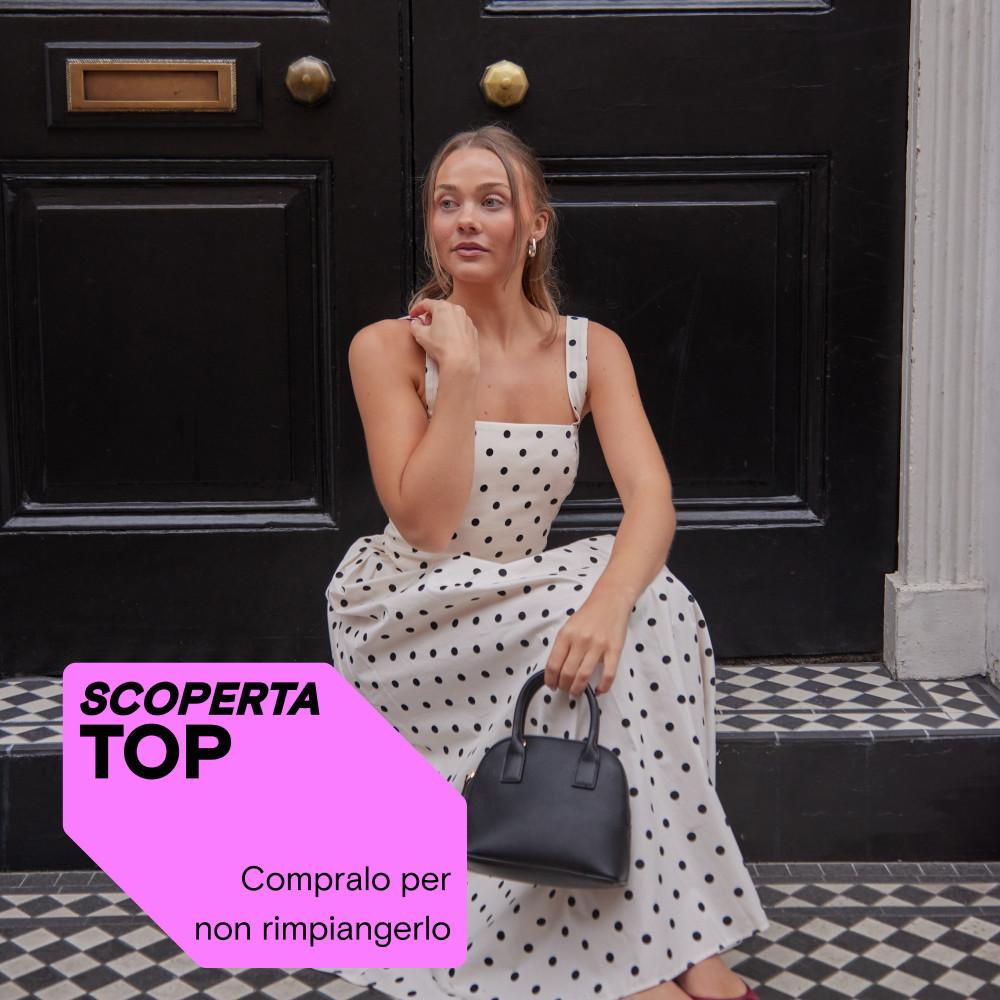 Modella seduta sui gradini di un edificio che indossa una tuta intera panna a pois e una borsetta nera.