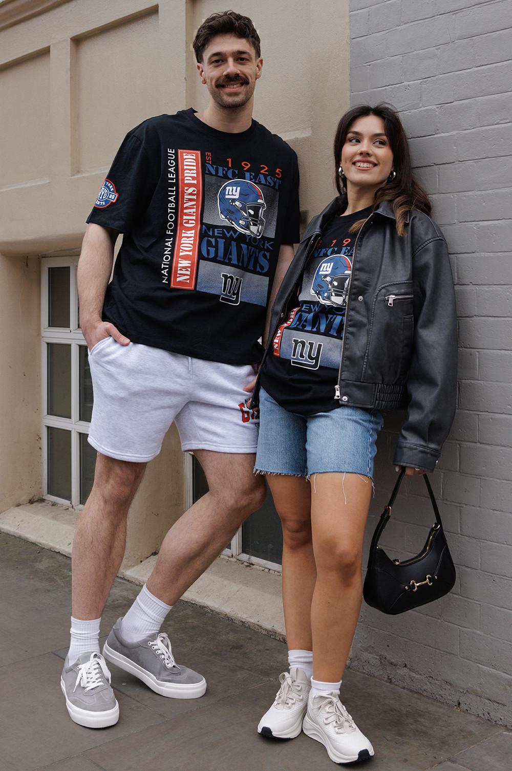 Two people wearing New York Giants T-shirts. One is in shorts, the other in denim shorts and a leather jacket.