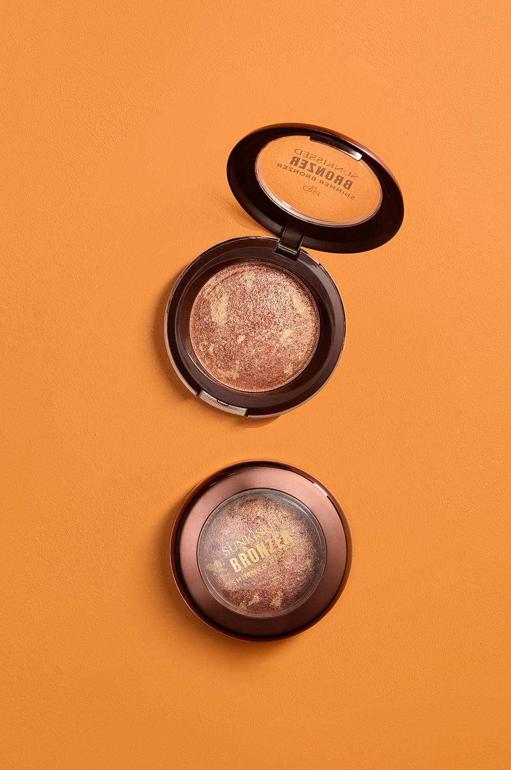 Due confezioni di terra abbronzante compatta su sfondo arancione, una aperta con la polvere glitterata in evidenza e una chiusa con la scritta "Sunkissed bronze shimmer".