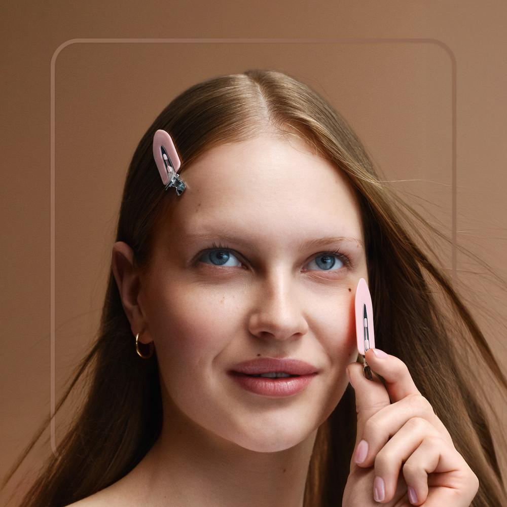 Modella che mostra i nuovi fermagli rosa: uno tra i capelli, l'altro in mano vicino al viso.