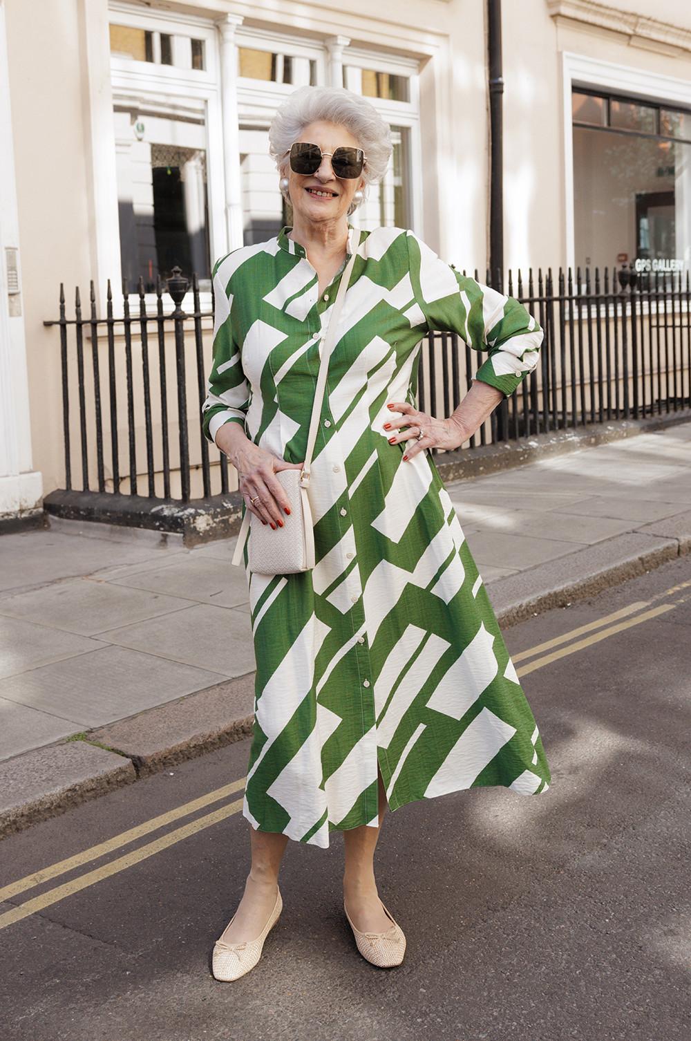 Model wearing green and white geometric print shirt dress with cream handbag and ballet flats, worn with oversized sunglasses.