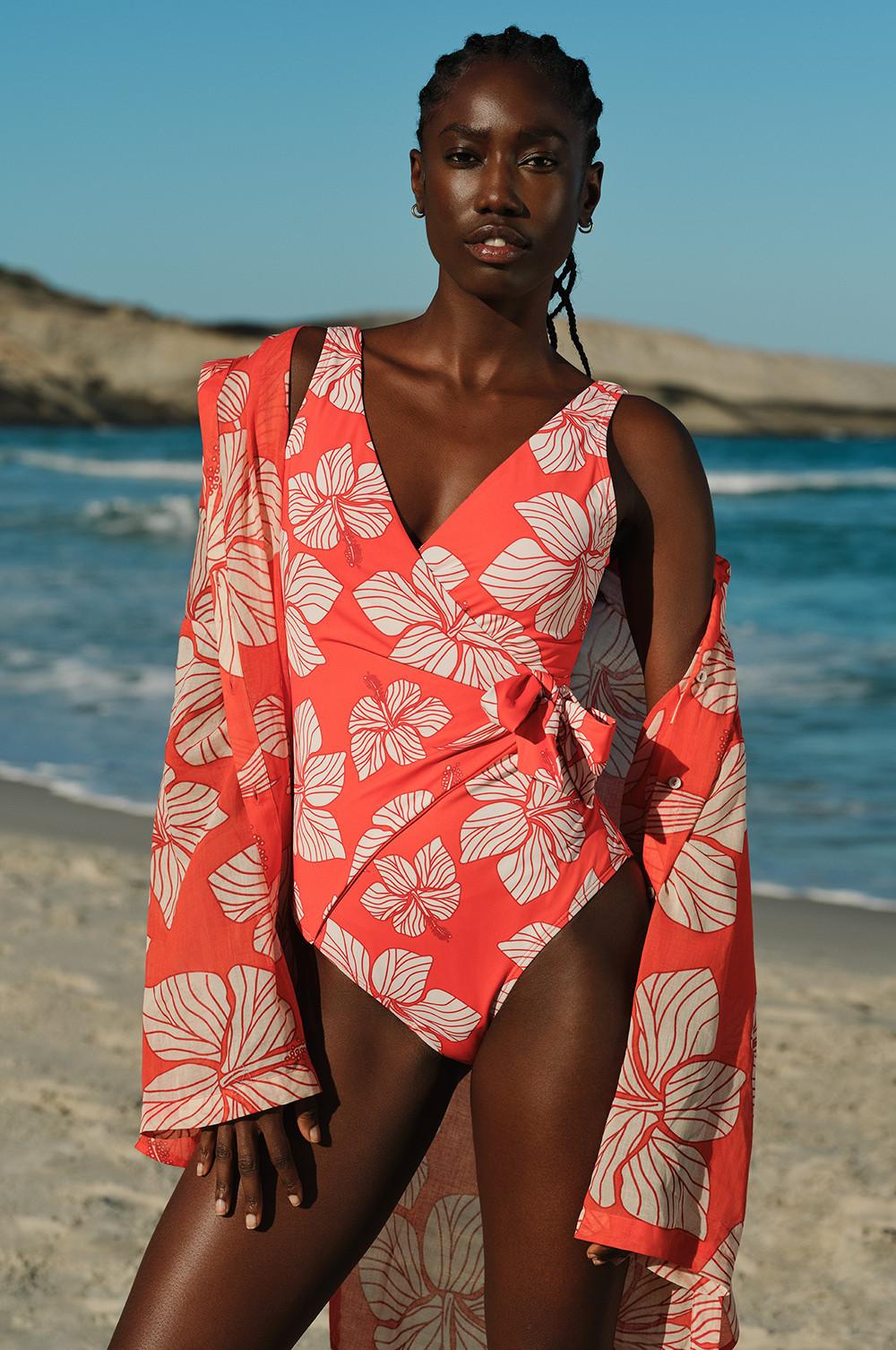 Maillot de bain corail à motif floral blanc porté avec la sortie de plage assortie, la plage en arrière-plan.
