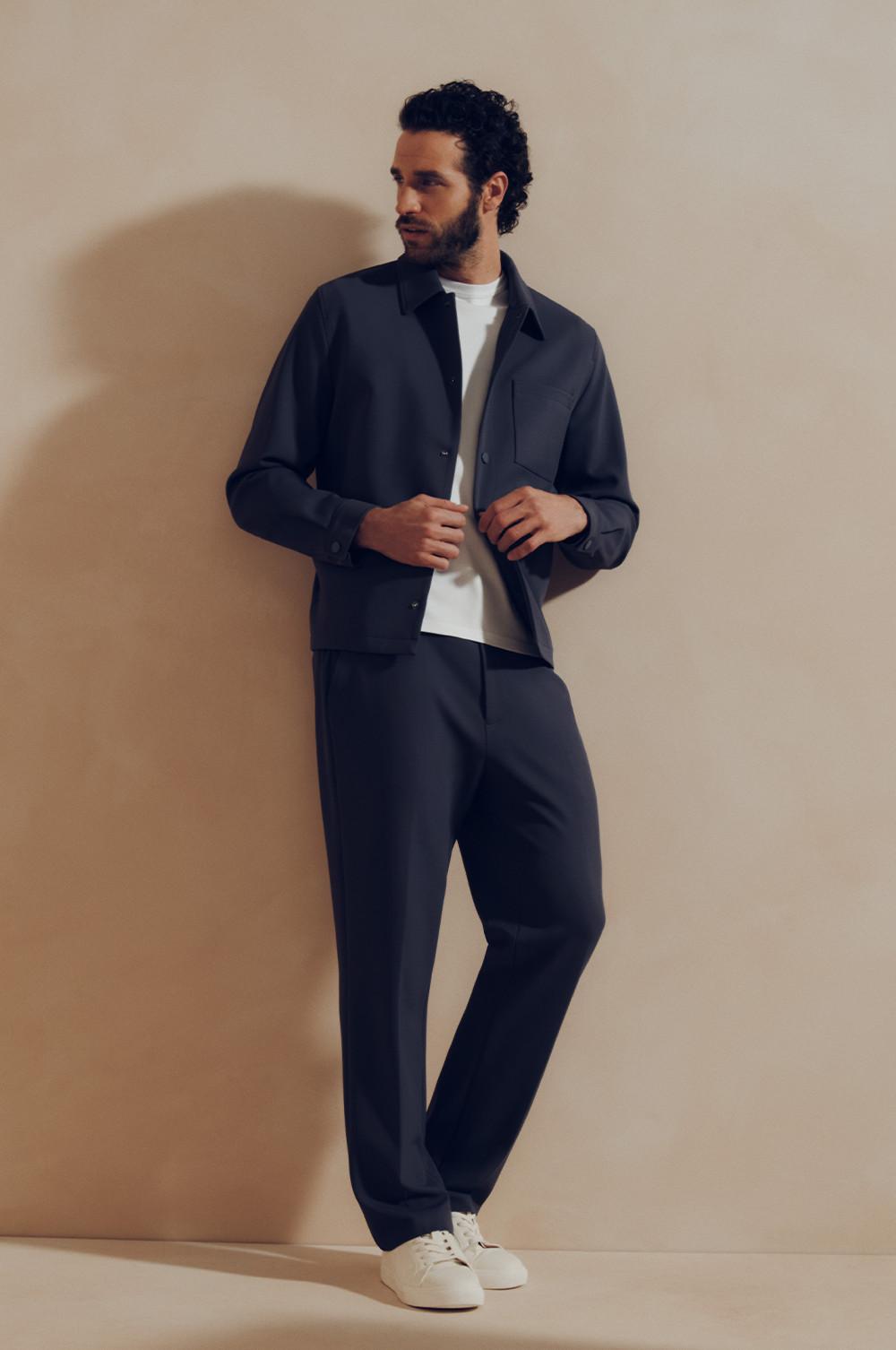 Model wearing navy shirt jacket over white t-shirt with matching navy trousers and white trainers.