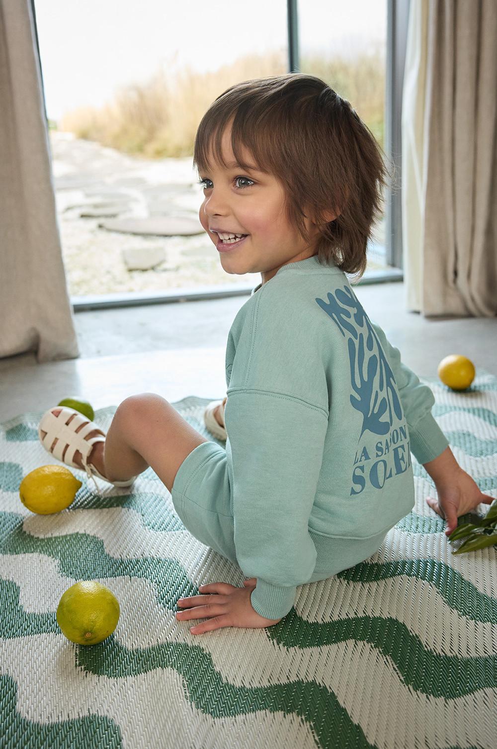 Niño con ropa para estar en casa, con sudadera y pantalones cortos en azul pastel y unas sandalias
