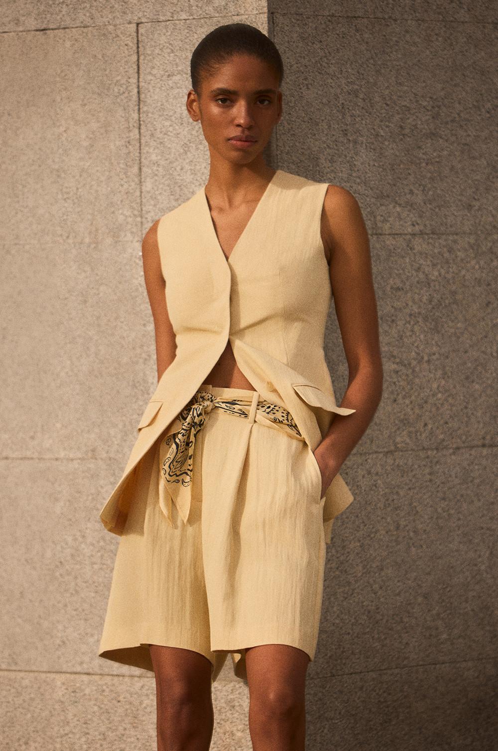 Model wearing cream sleeveless peplum top and matching tailored shorts with patterned belt.