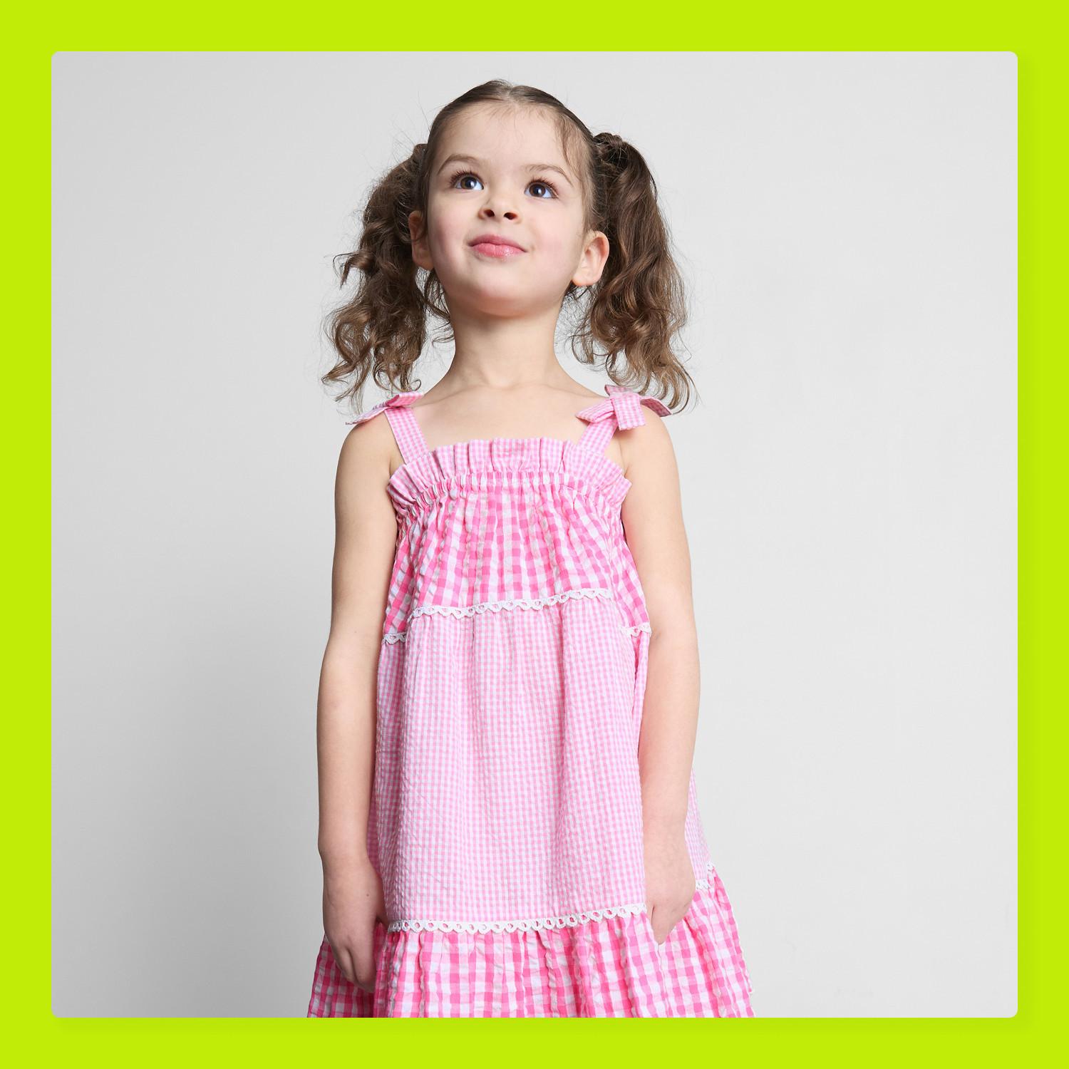 Young girl wearing yellow and white gingham dress with bow shoulder straps and scalloped hem.