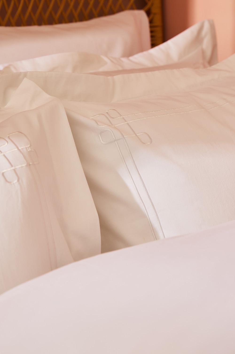 Cream bedding with embroidered decorative knot design on pillowcases and duvet cover.