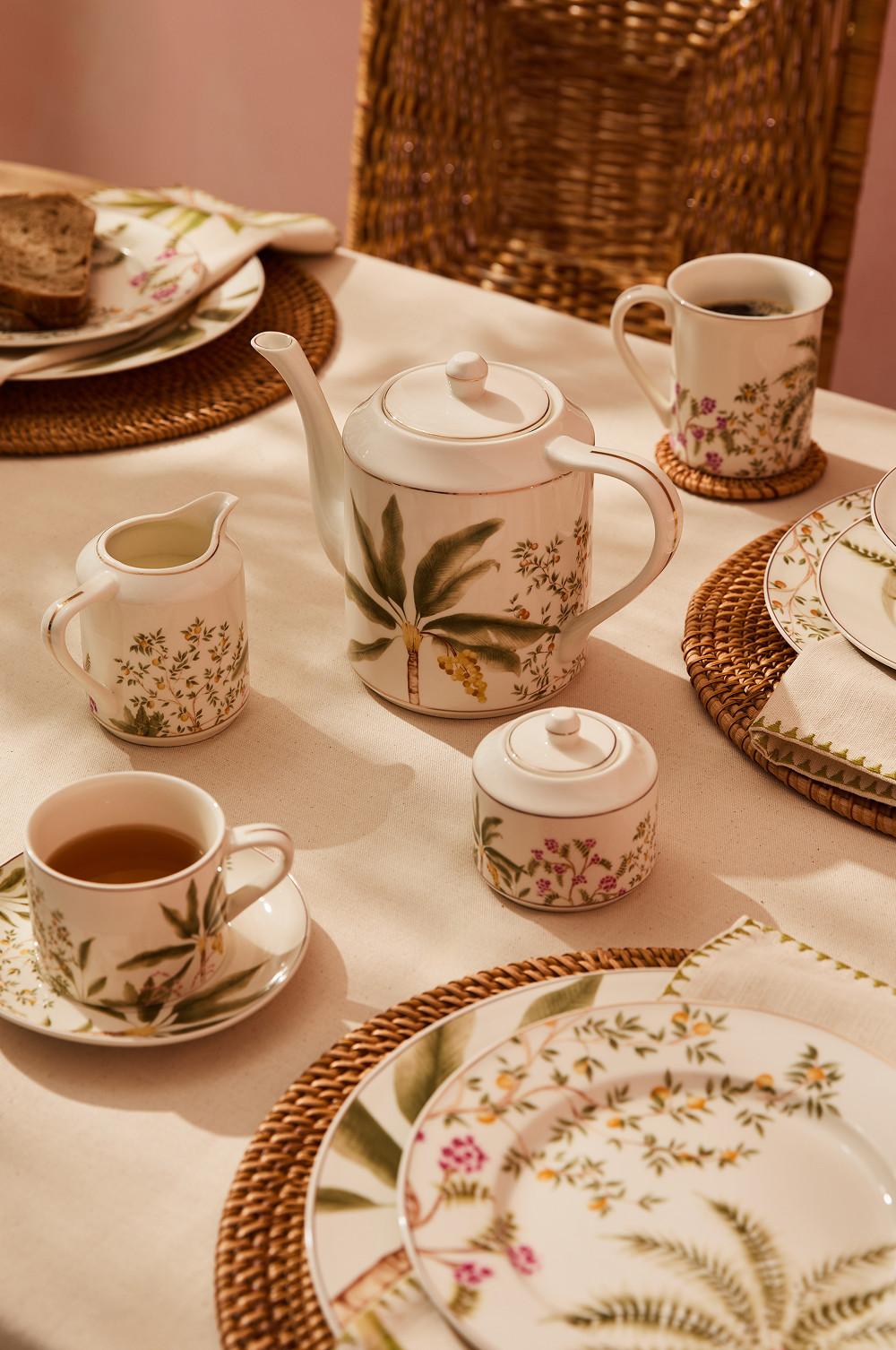 Botanical patterned tea set with teapot, cups, saucers and plates on woven placemats with afternoon tea.