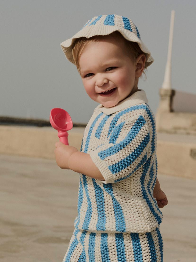 Child wearing grey and blue colour-block hooded jacket with matching dark trousers and blue trainers.