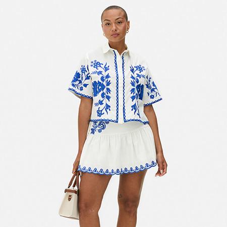 Model wears white skirt and cropped shirt with blue detail