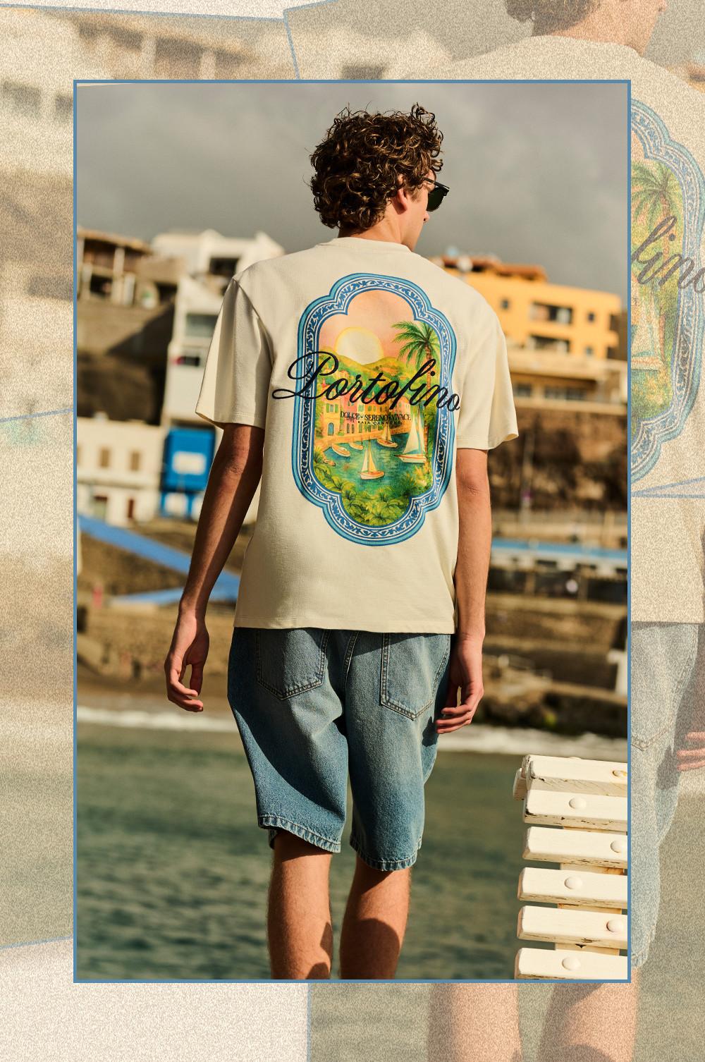 Back view of person wearing cream T-shirt with Portofino graphic print and denim shorts by the sea.