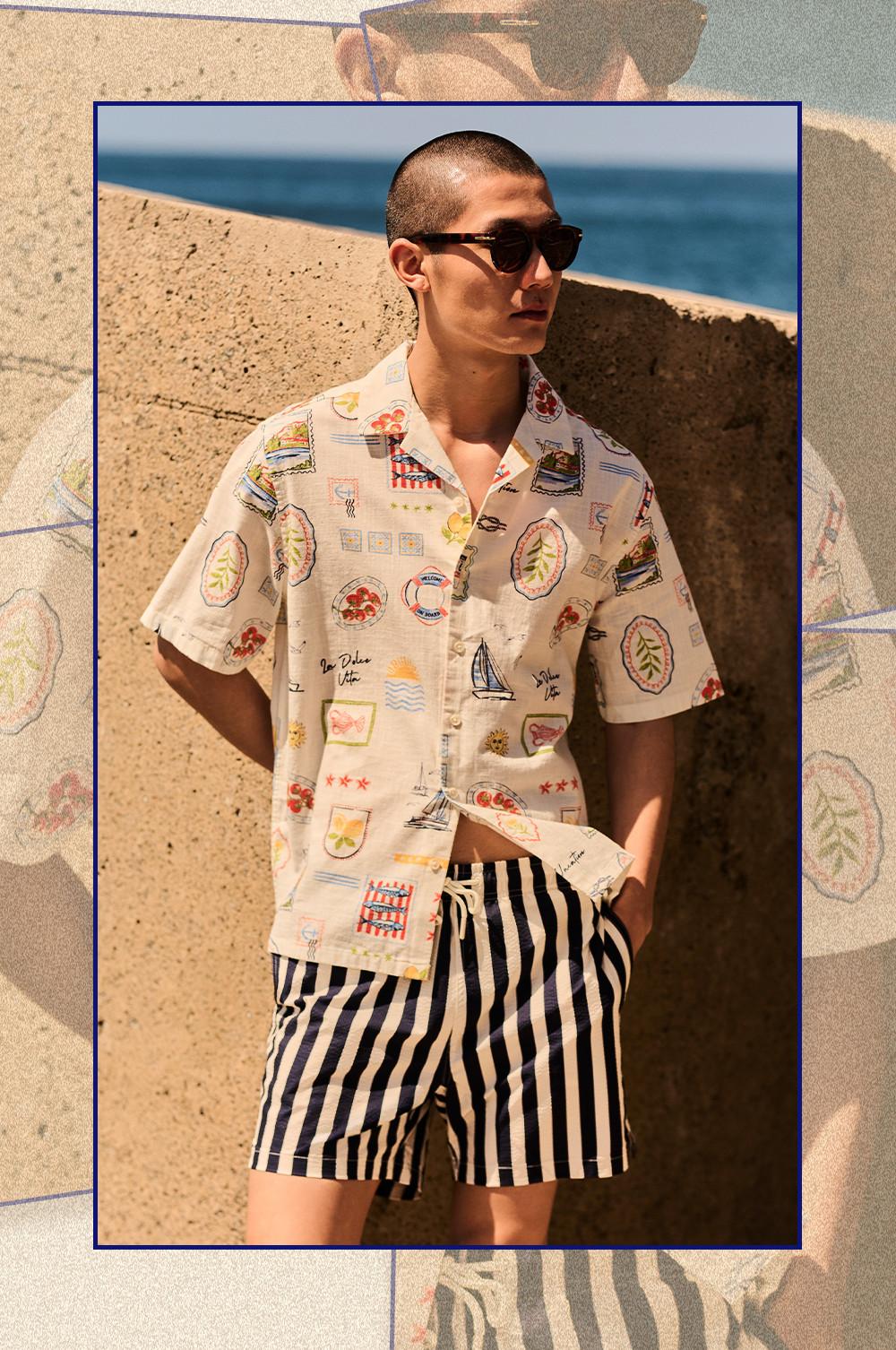 Model wearing sunglasses, cream short-sleeved shirt with colorful vacation print and black-and-white striped shorts.