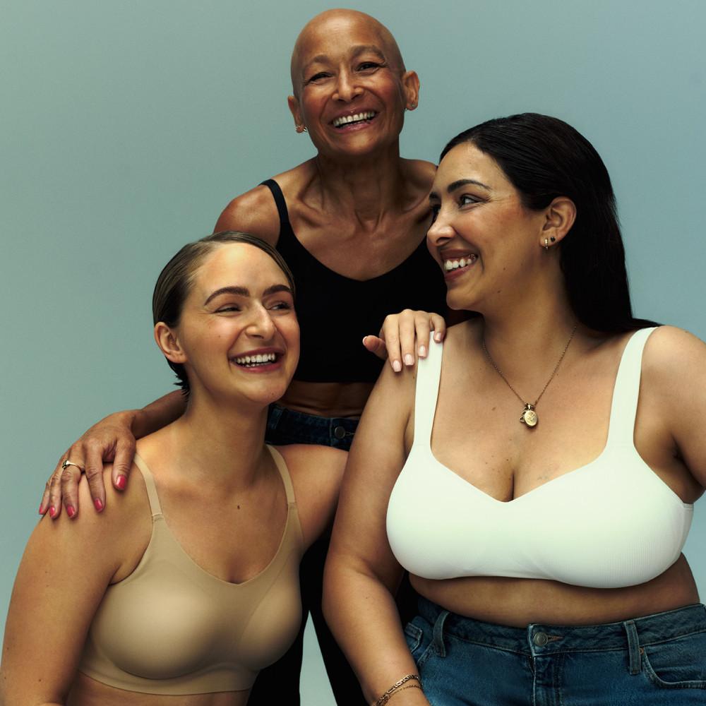 Drei Frauen unterschiedlichen Alters, die sich umarmen und lächeln, in beigen, schwarzen und weißen Bralettes.