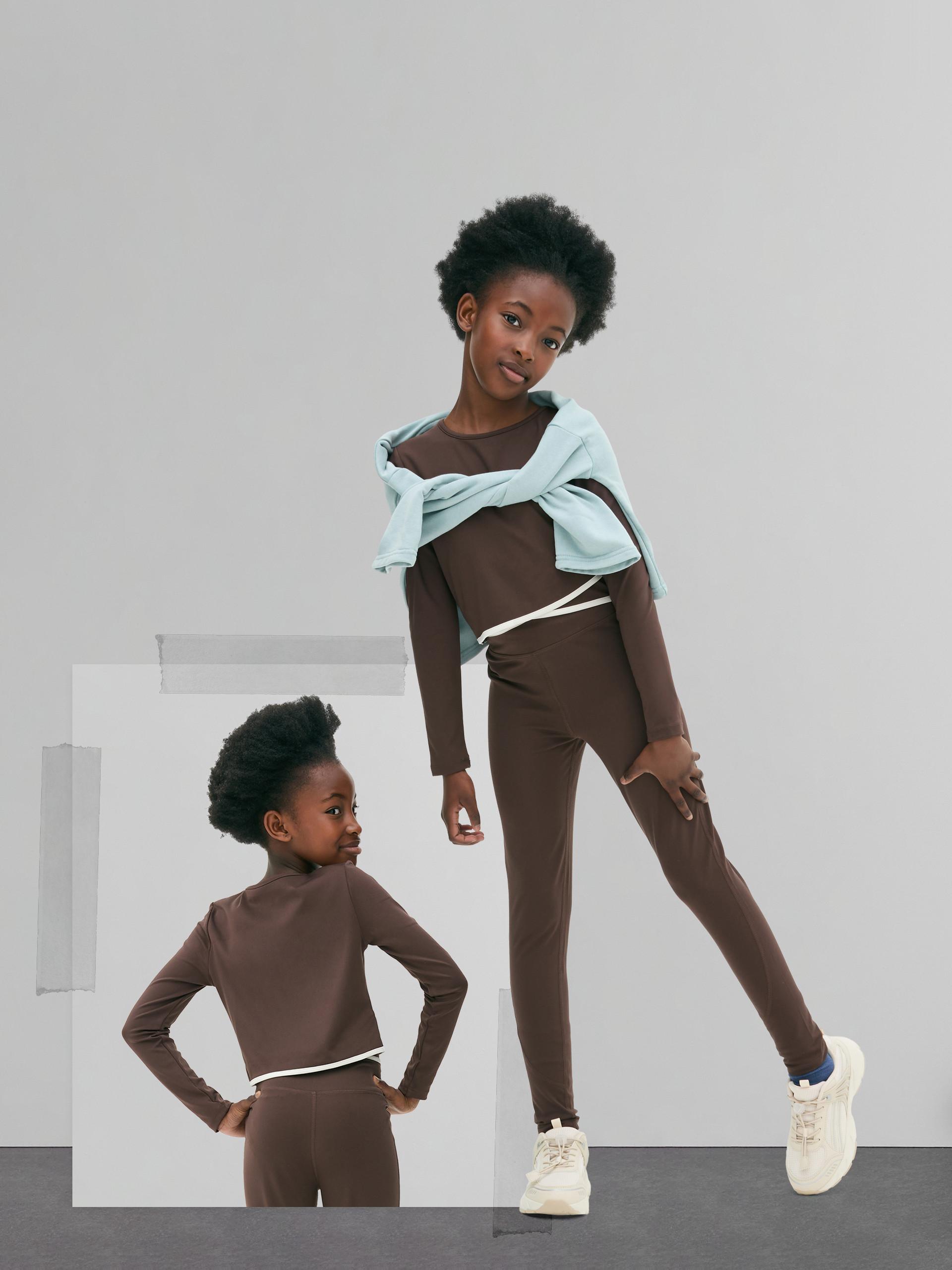Two people wearing matching brown athletic sets with white trim, one with a mint sweater tied around shoulders.