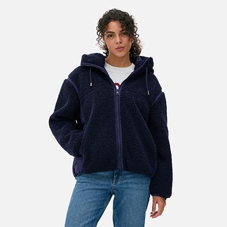 Navy blue teddy fleece hooded jacket with full zip front, worn with white top and blue jeans.
