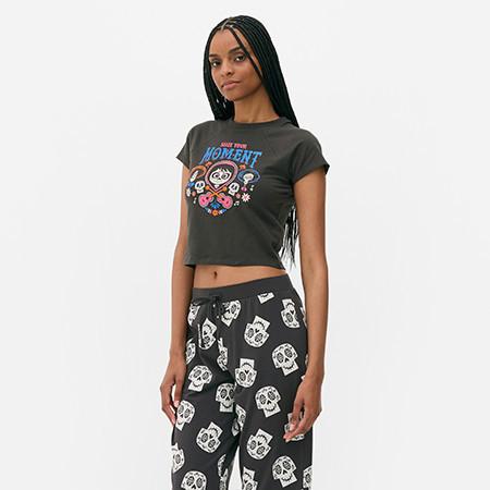Person wearing a grey crop top with cartoon graphics and black patterned trousers with skull prints.