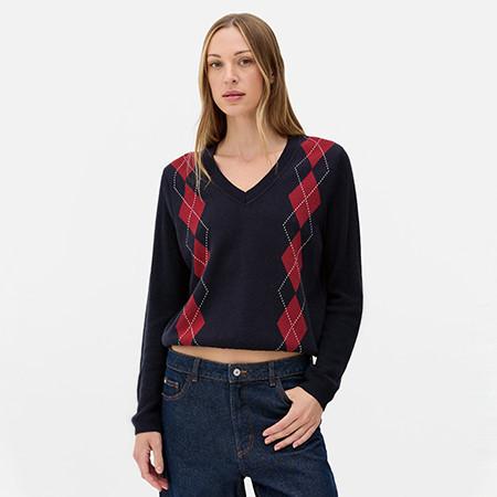 Person wearing a navy V-neck jumper with red argyle pattern, paired with dark denim jeans.