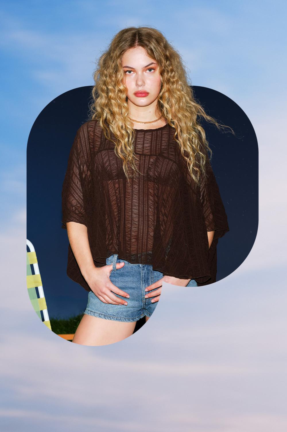 Woman wearing brown textured oversized top with gold necklace and denim shorts.