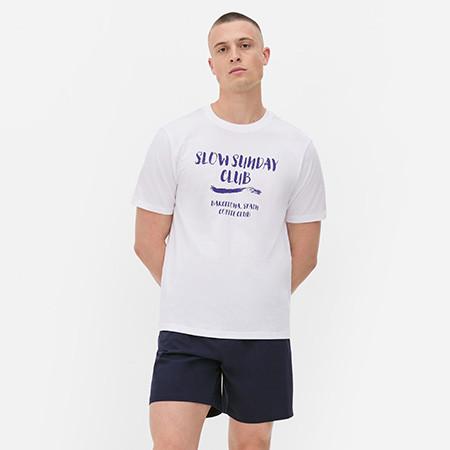 Person wearing white T-shirt with "Slow Sunday Club" blue text and navy shorts.