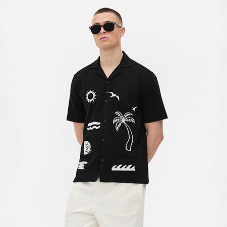 Person wearing black short-sleeve shirt with white beach-themed graphics and sunglasses.