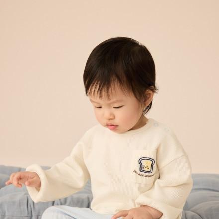 Young child wearing cream ribbed jumper with toast embroidery, sitting and looking down.