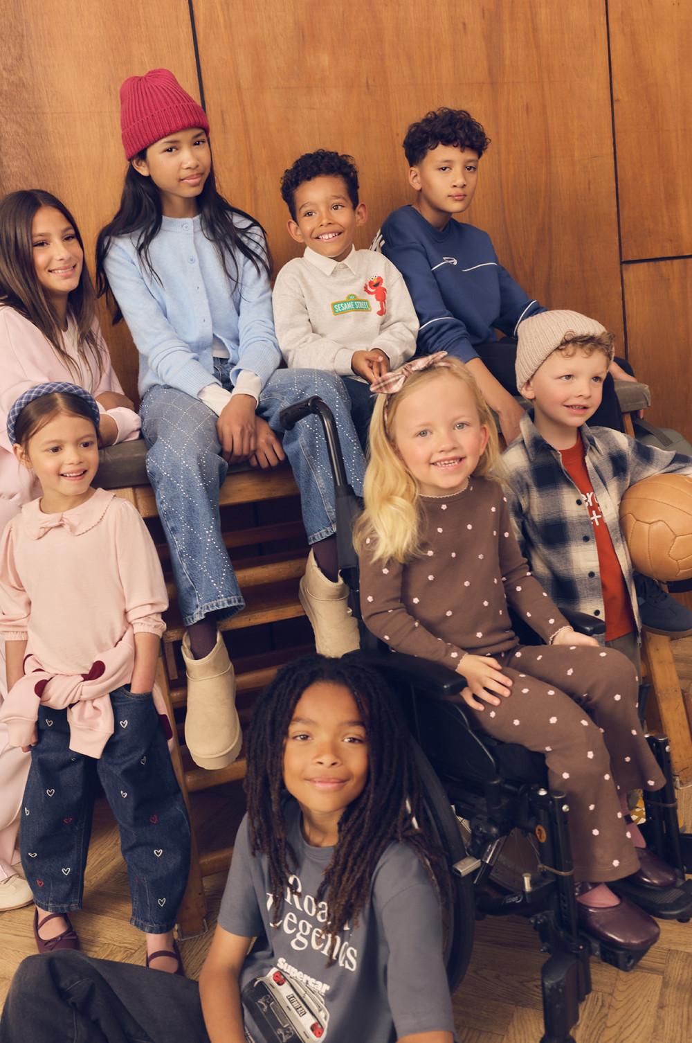 Group of children wearing casual fall clothing including knitted hats, hoodies and jeans, smiling together.