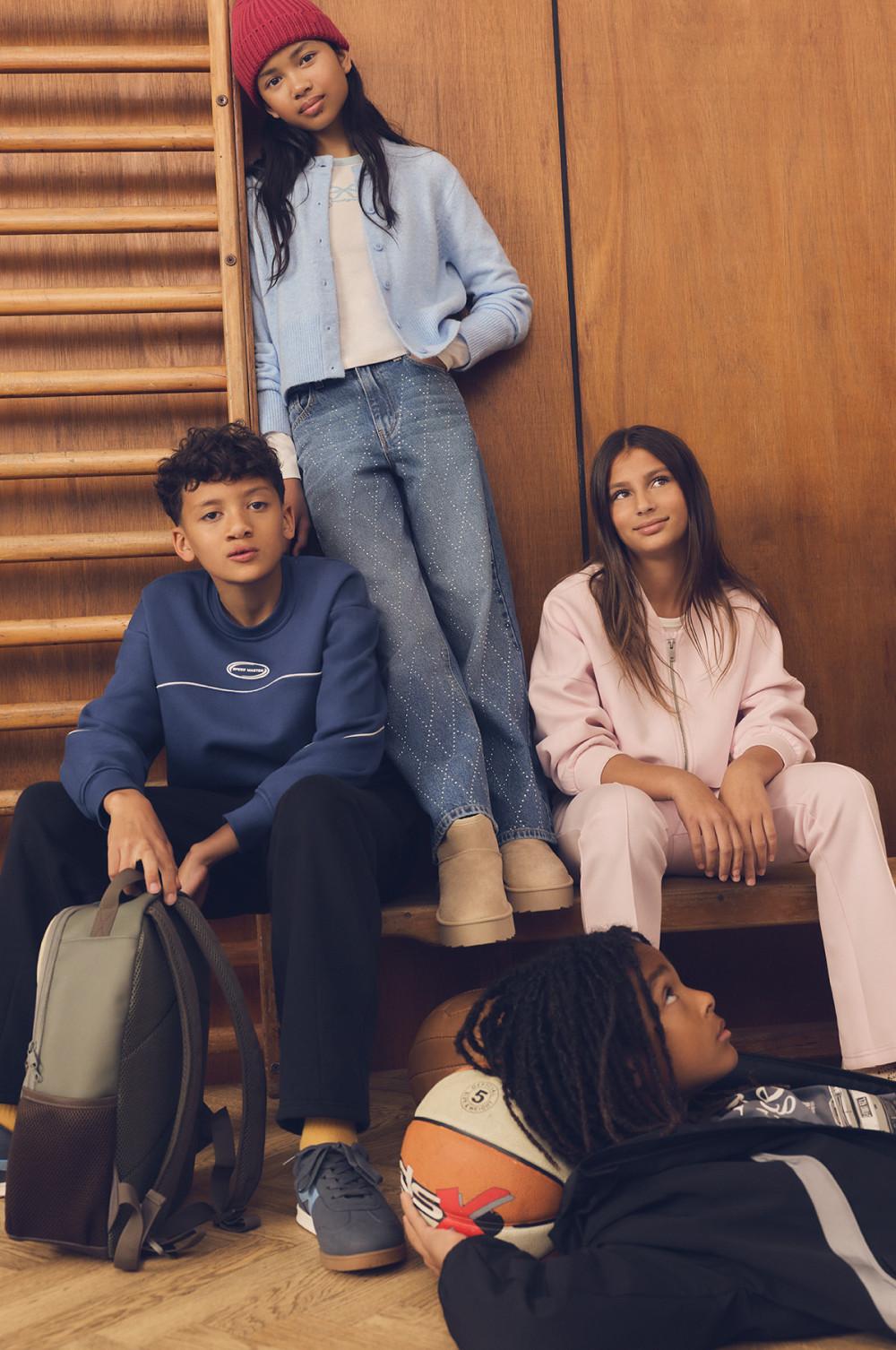 Four young people posing casually on wooden stairs wearing coordinated casual looks and sportswear.