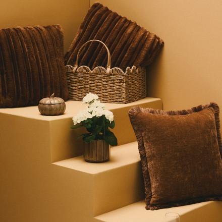 Brown ribbed velvet cushions displayed with woven basket, white flowers in vase and decorative box.
