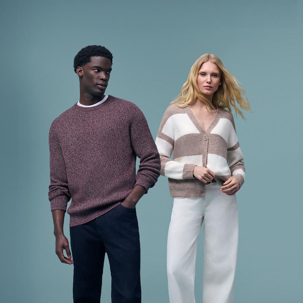 Twee modellen, één in een bordeauxrode trui met ronde hals en de ander draagt een gestreept vest op een witte broek.