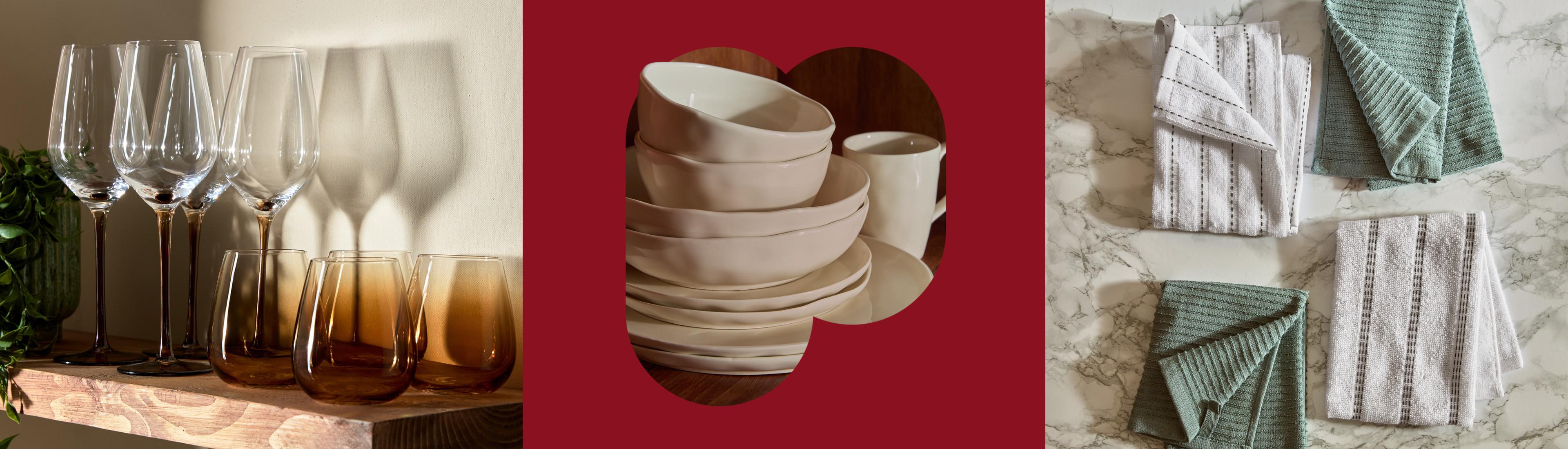 Ombre wine glasses in clear to amber, stacked cream ceramic dinnerware, and folded striped tea towels.