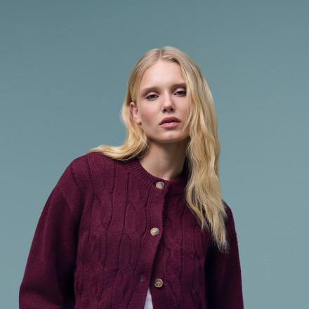 Woman wearing a burgundy cable-knit cardigan with button fastening.