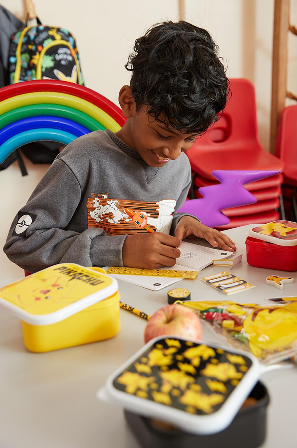 Enfant qui écrit dans un cahier avec plusieurs lunch boxes sur la table