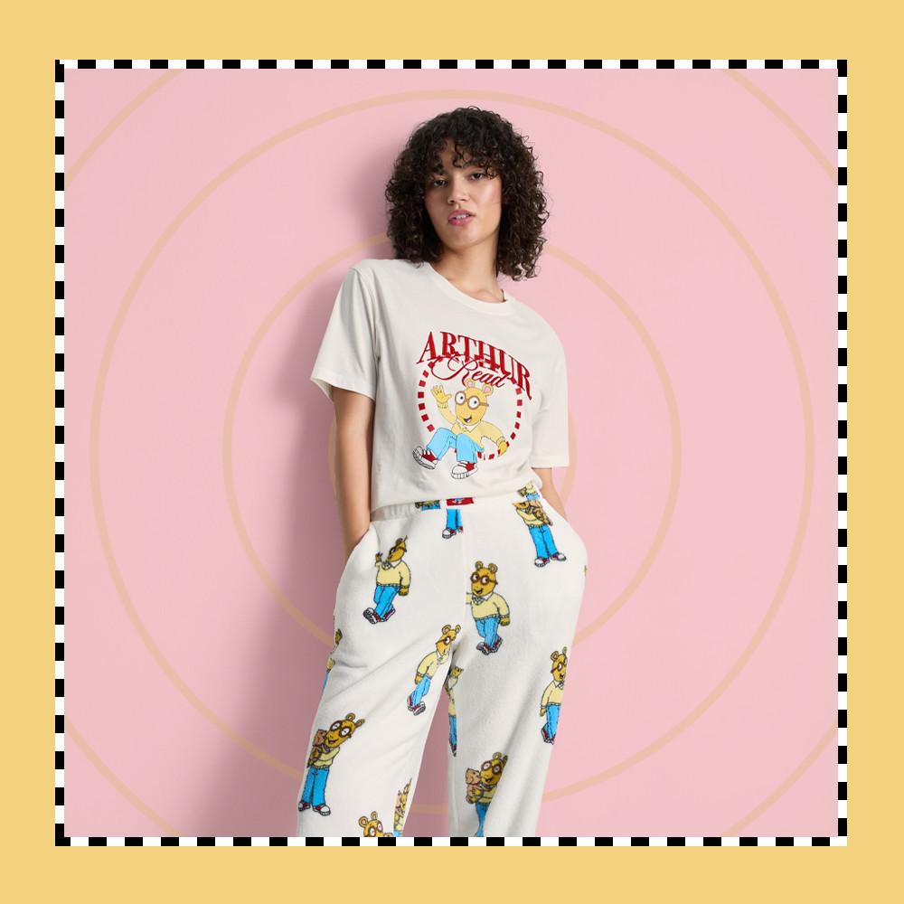 Donna che indossa una maglietta bianca con grafica e scritta "ARTHUR Read" e pantaloni del pigiama abbinati con stampa di personaggi.