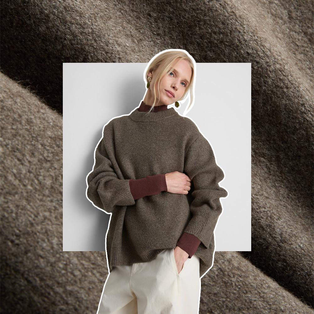 Model wearing an oversized olive green sweater with burgundy ribbed cuffs and cream pants.
