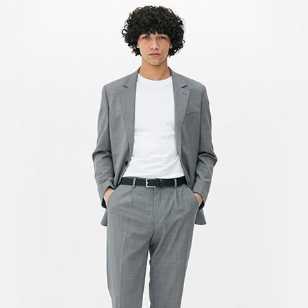 Person wearing a grey suit with matching trousers and white T-shirt standing with hands in pocket