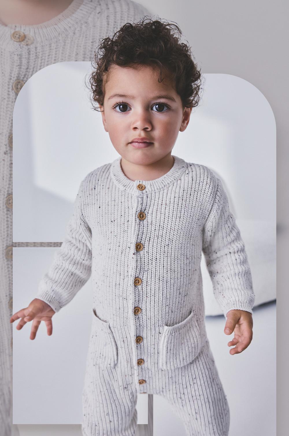 Young child wearing a gray knitted cardigan with wooden buttons and matching pants.