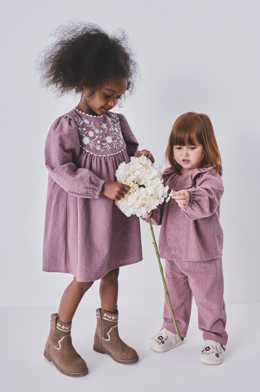 Two girls in purple outfits admiring a white hydrangea flower together.