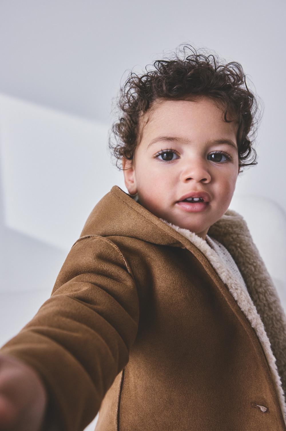 Toddler with curly hair wearing a brown fleece-lined hooded jacket.