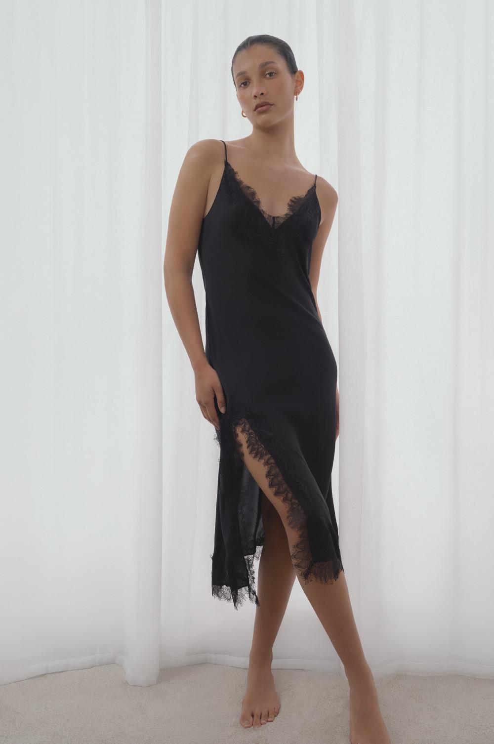 Model wearing a black slip dress with lace trim detailing on the neckline and asymmetric hem.